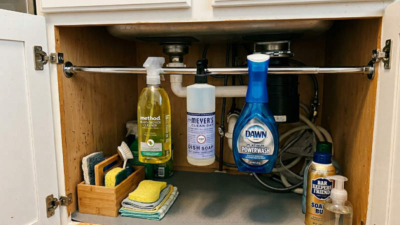 tension rod under kitchen sink holding spray bottles